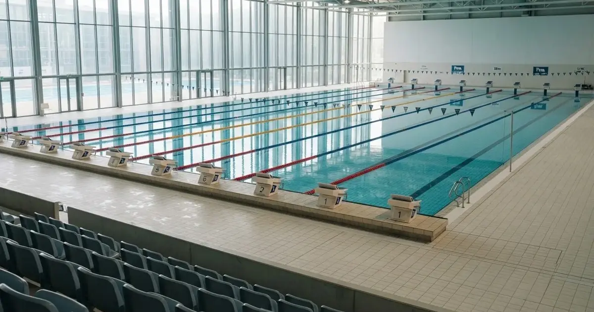 Pusty basen olimpijski z równymi torami i spokojną taflą wody, widok z trybun w jasnym świetle.