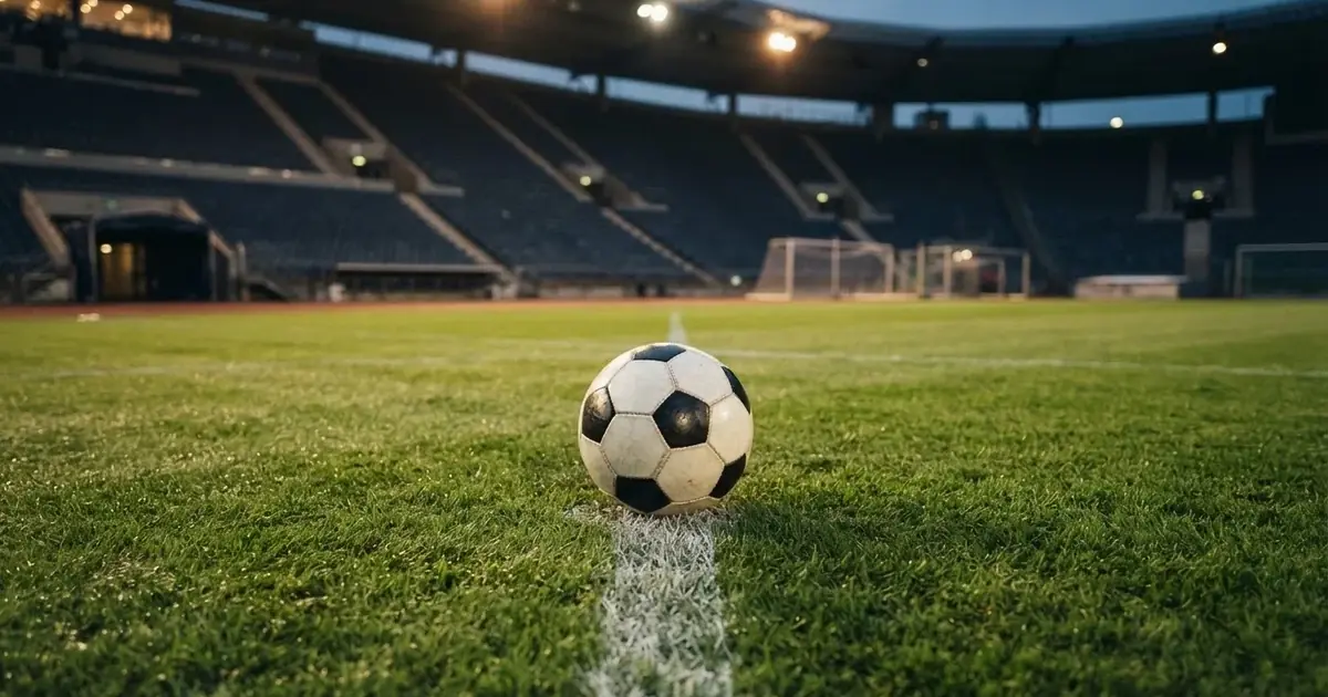 Piłka nożna leżąca na środku murawy w pustym stadionie przed meczem, rzędy siedzisk w półmroku.